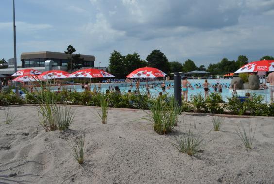 Freizeitbad mit Sandstrand, roten Sonnenschirmen und vielen Menschen im Schwimmbecken bei bewölktem Himmel